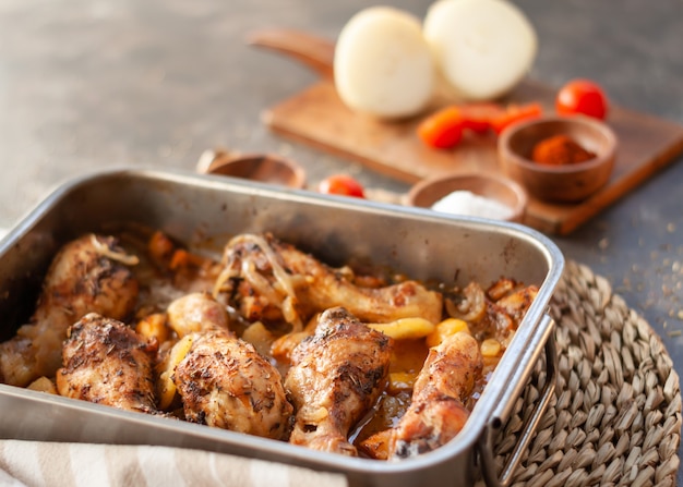 Cuisses de poulet rôti sur une plaque de cuisson en métal avec pommes de terre, oignons. tomates aux épices. Gros plan avec espace copie.