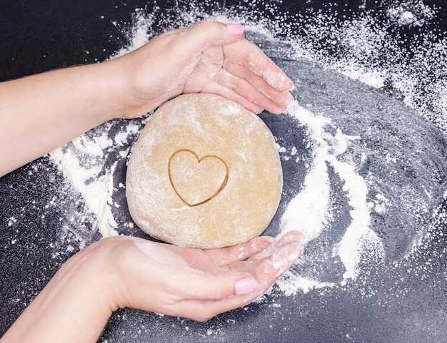 Cuisson des biscuits maison à partir de pâte en forme de coeur et mot amour sur fond noir