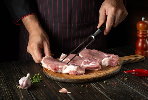 Cuisson des côtes de viande crue par les mains du chef dans la cuisine du restaurant La main du cuisinier tient une fourchette Délicieux déjeuner grillé