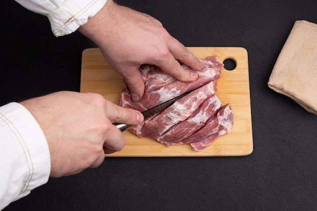 Cuisson du steak de porc juteux par les mains du chef sur fond noir foncé.
