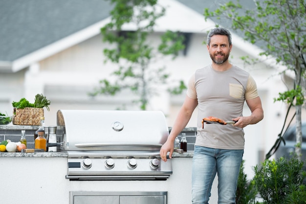 La cuisson des hommes sur un barbecue dans la cour faire cuire à un barbecue la préparation de la viande guy cuisson de la viande sur ba