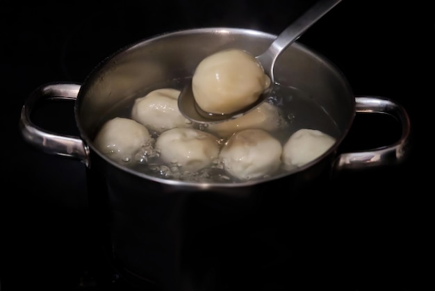 Cuisson des khinkals dans de l'eau bouillante Khinkali bouilli dans une casserole le cuisinier mélange les boulettes avec une cuillère dans une casserole en gros plan