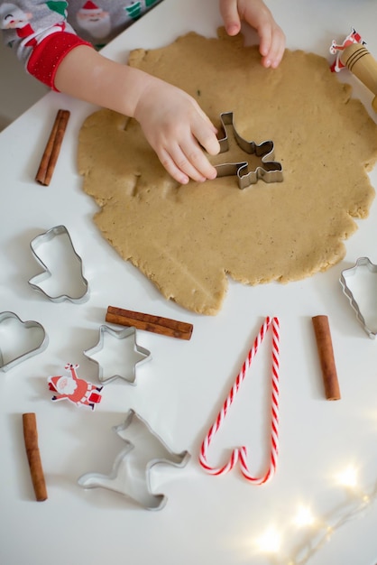 Cuisson de Noël fond pâte emporte-pièces épices et décorations de Noël Enfant faisant des biscuits avec des emporte-pièces Biscuits de Noël sur un tableau blanc