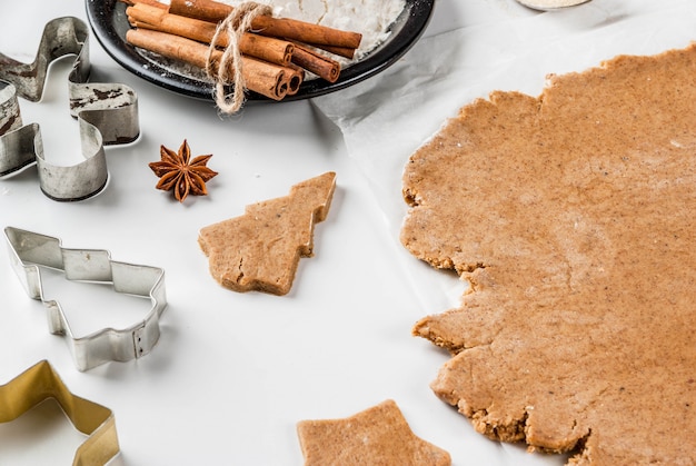 Photo cuisson de noël pâte de gingembre pour pain d'épice hommes de pain d'épice étoiles arbres de noël rouleau à pâtisserie épices (cannelle et anis) farine sur la table de marbre blanc de cuisine à domicile