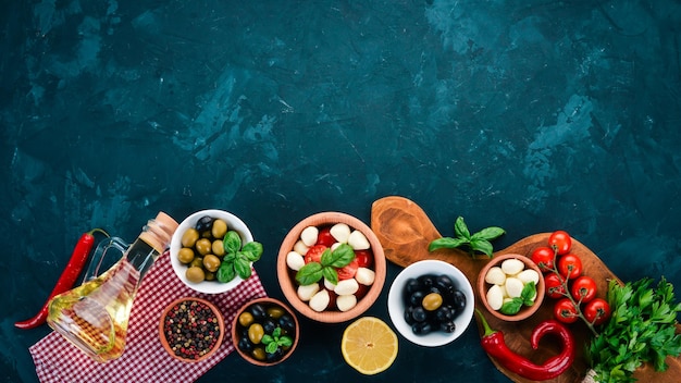 La cuisson d'une salade caprese fromage mozzarella tomates cerises olives feuilles de basilic huile poivre sur une table en pierre noire espace libre pour le texte