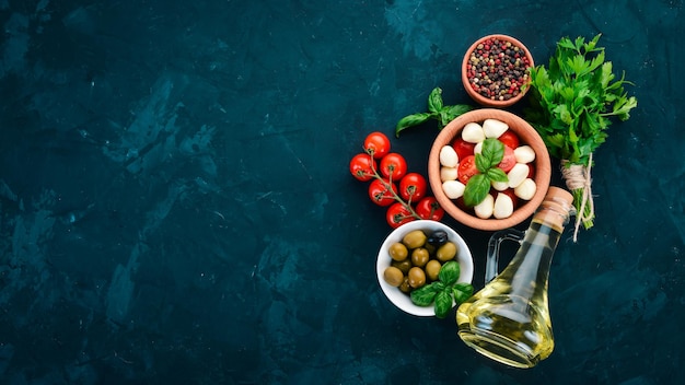 La cuisson d'une salade caprese fromage mozzarella tomates cerises olives feuilles de basilic huile poivre sur une table en pierre noire espace libre pour le texte