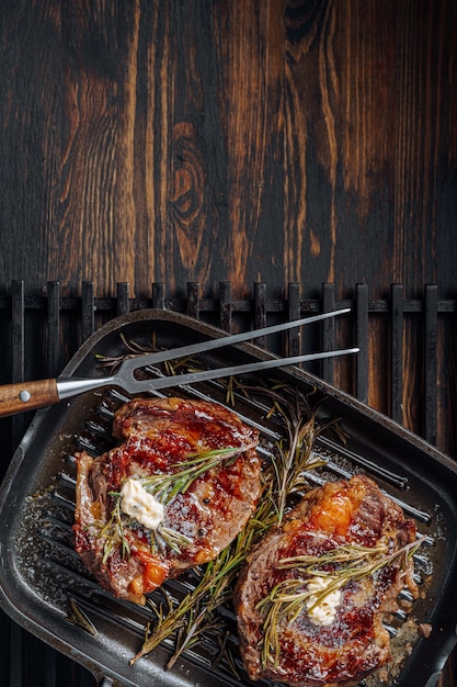 Cuisson de somptueux steaks dans une poêle à griller avec du beurre étalé sur le steak assaisonné de poivre moulu et de sel avec des brins de romarin