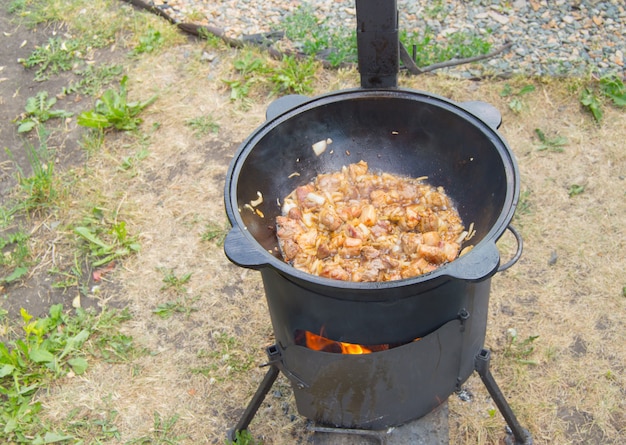 Cuisson de la viande frite dans une grande poêle à frire sur la cuisinière avec un feu ouvert, dîner en famille à l'extérieur, gros plan