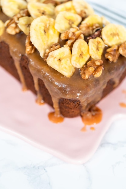 Cuit fraîchement une miche de pain aux noix de banane arrosée de caramel maison sur une planche à découper rose.