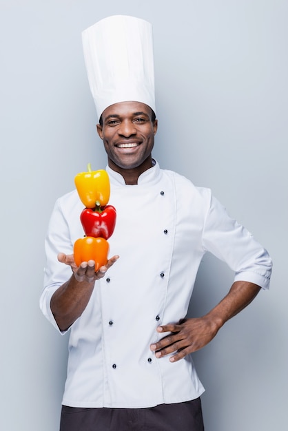 culinaire coloré. jeune chef africain confiant en uniforme blanc tenant des poivrons multicolores