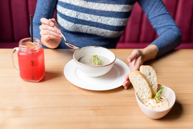 Culture de femme tenant une cuillère et un bol blanc de soupe à la crème de champignons.