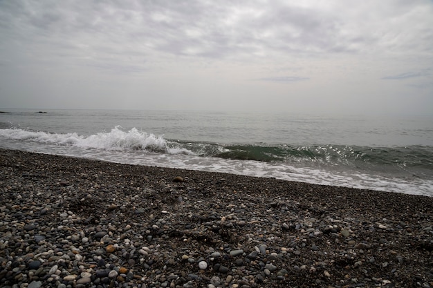 Écume de mer blanche sur une plage de galets rocheux, marée haute, tempête