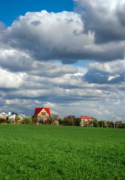 Cumulus lumineux un jour de printemps Champ vert de blé d'hiver et un village à l'horizon