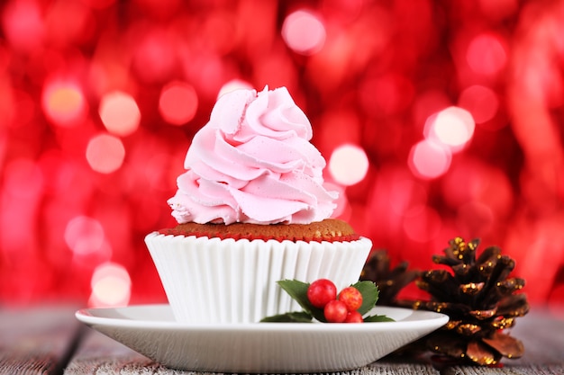 Cup-cake à la crème sur soucoupe et décoration de Noël sur table en bois et fond brillant