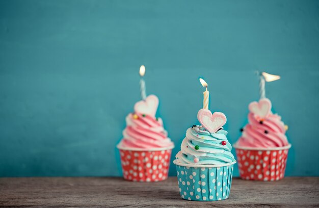 cupcake d&#39;anniversaire avec la forme de coeur de guimauve et bougie sur fond bleu