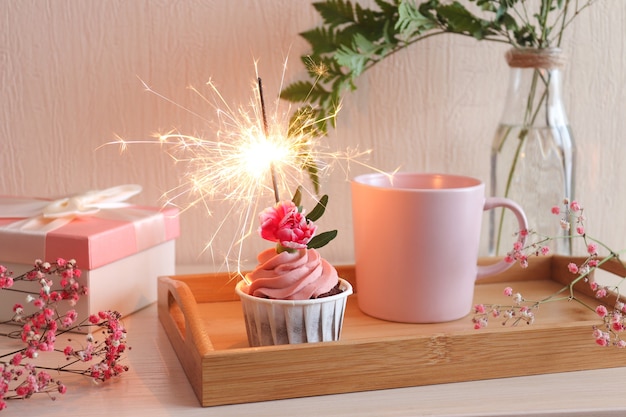 Cupcake d'anniversaire de temps de fête avec sparkler, tasse de café sur un plateau en bois