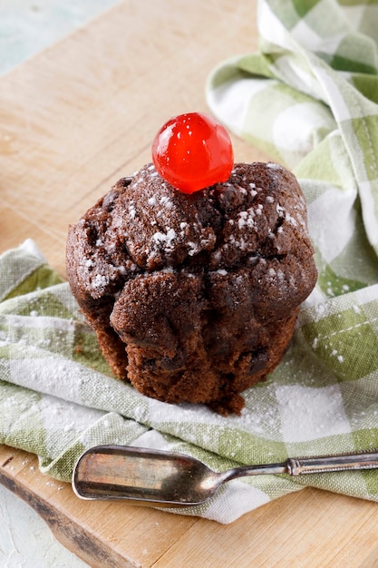 Cupcake au chocolat avec glaçage sur serviette sur planche de bois et vieille cuillère