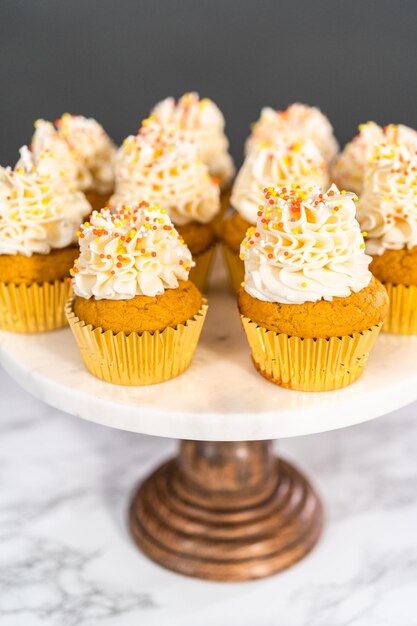 Cupcake aux épices à la citrouille avec crème au beurre italienne et pépites sur un présentoir à gâteaux.