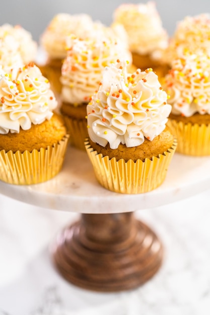 Cupcake aux épices à la citrouille avec crème au beurre italienne et pépites sur un présentoir à gâteaux.