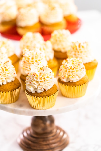 Cupcake aux épices à la citrouille avec crème au beurre italienne et pépites sur un support à gâteau.