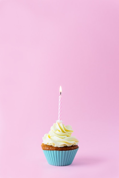 Cupcake avec une bougie sur fond rose