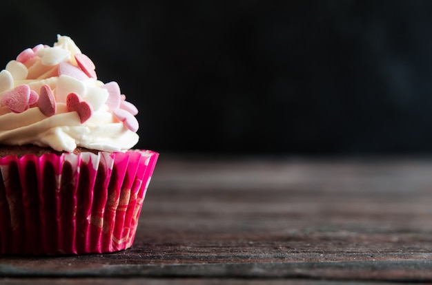 Cupcake festif pour la Saint Valentin sur fond noir en bois avec des coeurs.