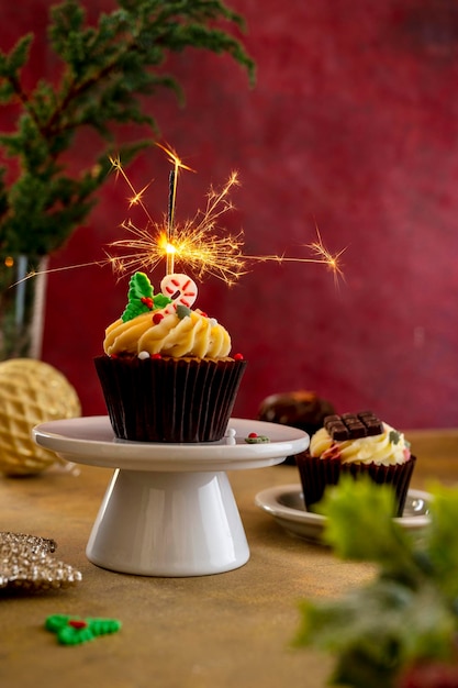 Cupcake de Noël avec sparkler sur cake stand fond bordeaux coloré image de style de vie Moody