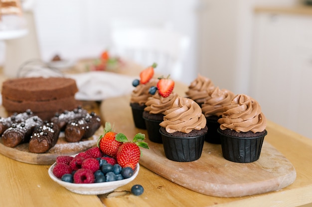 Cupcakes au caramel au chocolat sur planche de bois, baies sur assiette, génoise, gâteau aux pommes de terre sur la table