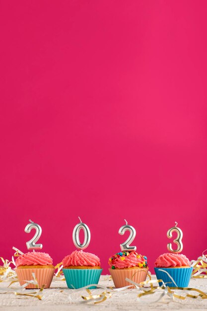 Cupcakes et bougies de fête sous forme de nombres 2023 sur fond rose Concept de cadre vertical du nouvel an