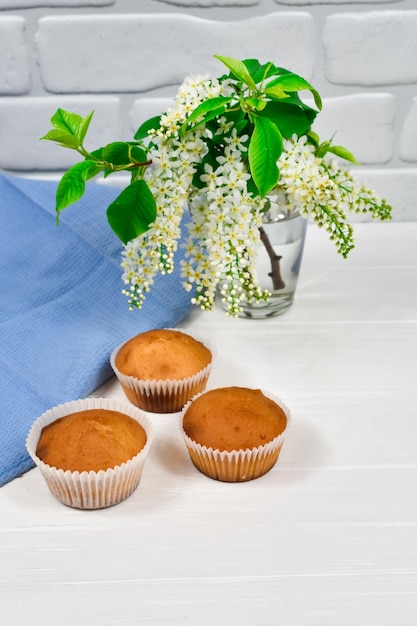 Cupcakes avec un bouquet de fleurs blanches Cupcakes sur une assiette blanche avec une nappe bleue et un bouquet de fleurs sur une table en bois blanc