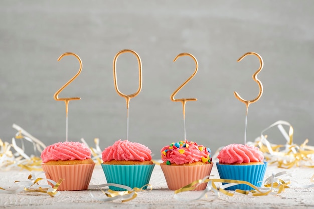 Cupcakes du Nouvel An et cierges dorés numéros 2023 muffins de vacances avec glaçage au beurre rose fond gris