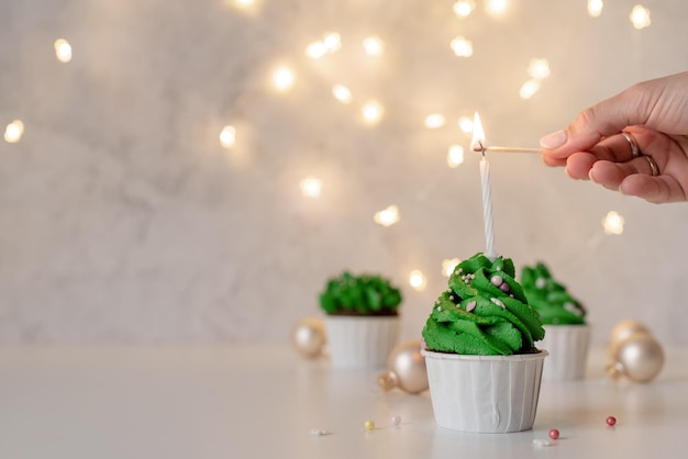 Cupcakes en forme d'arbre de Noël, entourés de décorations festives et de lumières en arrière-plan