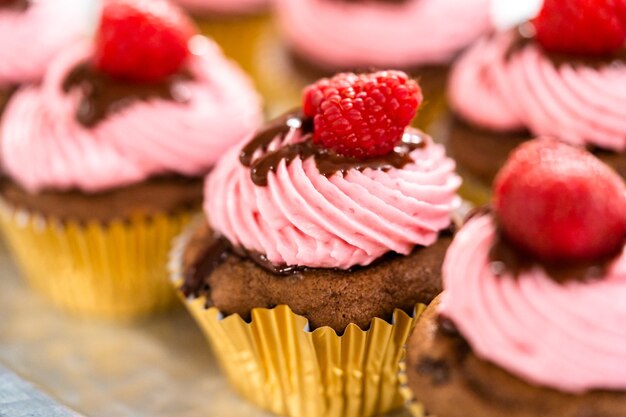 Cupcakes gourmands au chocolat et aux framboises arrosés de ganache au chocolat et surmontés d'une framboise fraîche.