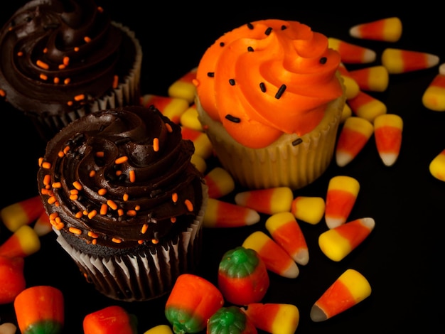 Cupcakes Halloween orange et noir avec des bonbons au maïs sur fond noir.