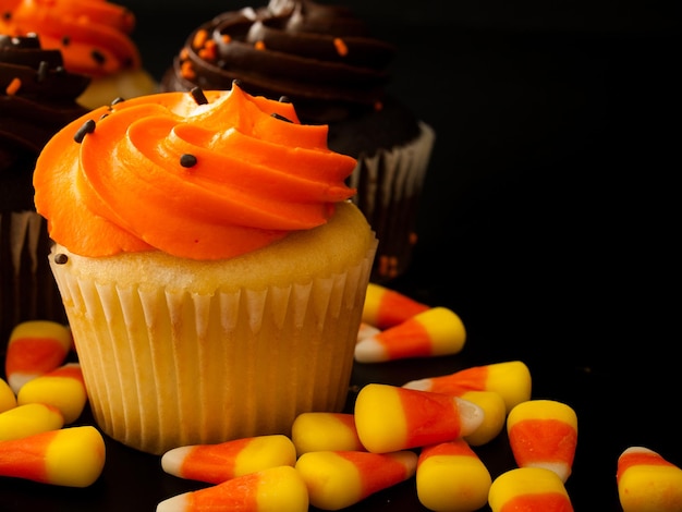 Cupcakes Halloween orange et noir avec des bonbons au maïs sur fond noir.