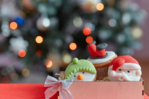 Cupcakes de Noël confortables et esthétiques dans une boîte en bois Cadeau devant le bokeh de l'arbre de Noël Bonne ambiance de vacances Mise au point sélective