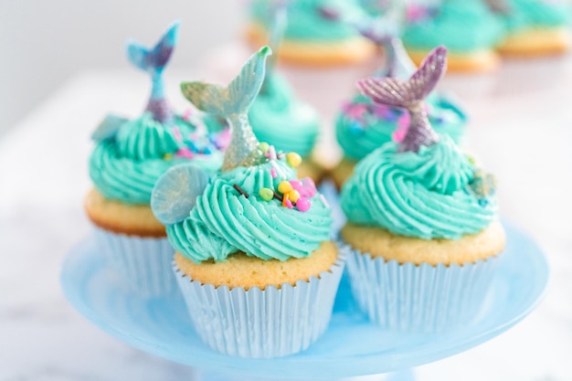 Cupcakes de sirène gastronomiques garnis d'un glaçage à la crème au beurre bleu et décorés de vermicelles et de queues de sirène au chocolat.