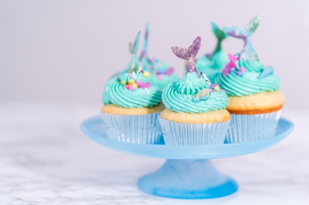 Cupcakes de sirène gastronomiques garnis d'un glaçage à la crème au beurre bleu et décorés de vermicelles et de queues de sirène au chocolat.