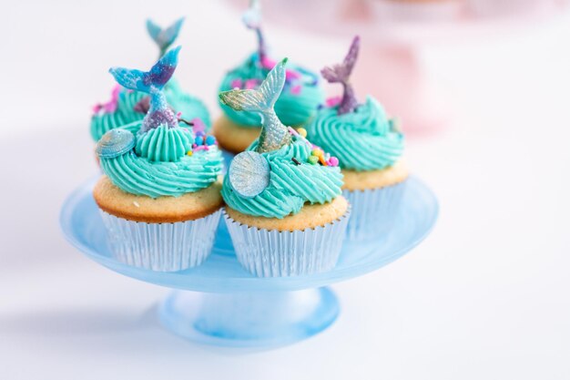 Cupcakes de sirène gastronomiques garnis d'un glaçage à la crème au beurre bleu et décorés de vermicelles et de queues de sirène au chocolat.