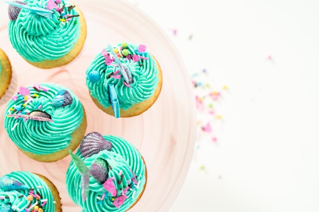 Cupcakes de sirène gastronomiques garnis d'un glaçage à la crème au beurre bleu et décorés de vermicelles et de queues de sirène au chocolat.