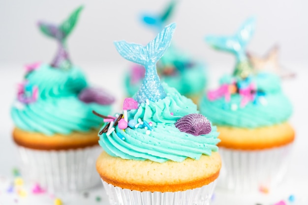 Cupcakes de sirène gastronomiques garnis d'un glaçage à la crème au beurre bleu et décorés de vermicelles et de queues de sirène au chocolat.