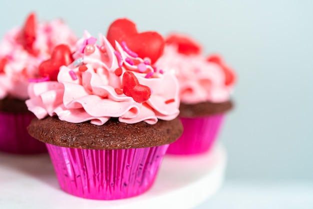 Cupcakes en velours rouge avec glaçage à la crème au beurre italien rose et décor de chocolats rouges en forme de cœur et de baiser.