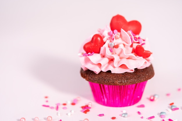 Cupcakes en velours rouge avec glaçage à la crème au beurre italienne rose et décorés de chocolats rouges en forme de cœur et de baiser.