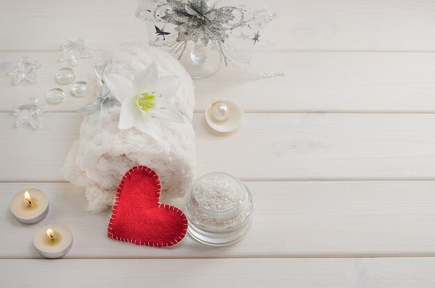 Cures thermales pour la Saint Valentin. Serviette blanche avec fleur et perles sur une table en bois blanche avec un coeur rouge et des bougies avec espace copie. Salon de beauté, massage.