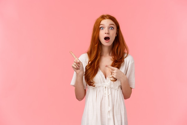 Curieuse et excitée, séduisante fille de gingembre séduisante en robe blanche, parle de réductions incroyables