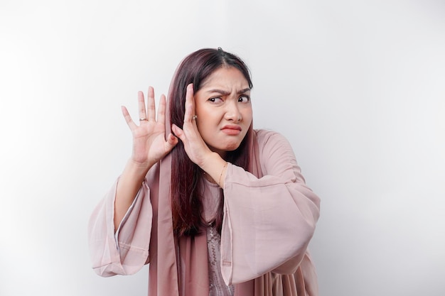 Une curieuse jeune femme musulmane asiatique portant un foulard essayant de vous entendre entendre écouter attentivement isolé sur fond blanc