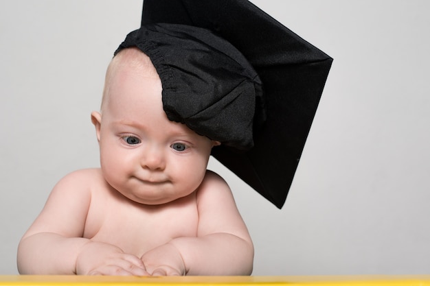 Curieux bébé au chapeau académique à la table. Concept pédagogique