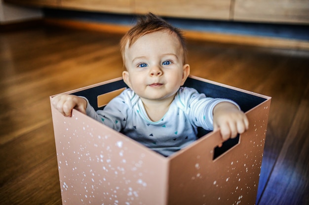 Curieux enfant en bas âge caucasien blond mignon avec de beaux yeux bleus assis dans la boîte