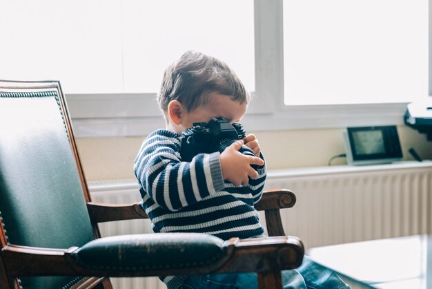 Curieux enfant explore la caméra assis sur une chaise