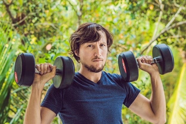 Curl de biceps - homme de remise en forme de musculation à l'extérieur travaillant des bras soulevant des haltères faisant des boucles de biceps. Modèle sportif masculin exerçant à l'extérieur dans le cadre d'un mode de vie sain.